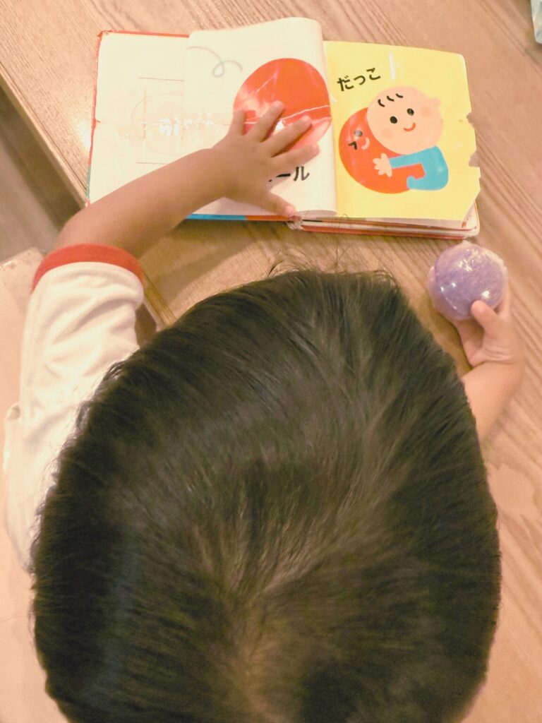 厚いボードブックのページを自分でめくっている子ども